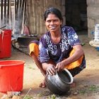 Woman sitting on the ground with a claypot, outside a building.