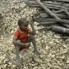 Senegalese boy in sitting amongst a mass of oyster shells and wood collected in a mangrove forest